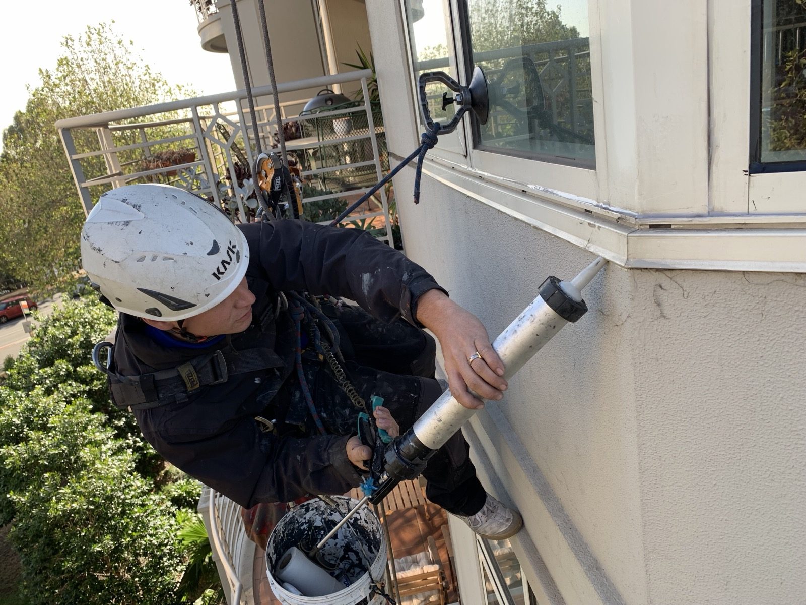 Mission Possible technician applying sealant to a window frame while suspended on rope